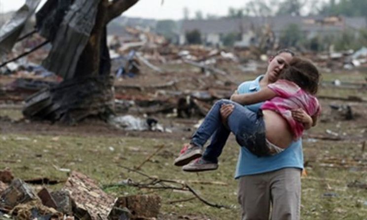 A woman carries a child through a field near the collapsed Plaza Towers Elementary School - Sue Ogrocki (The Associated Press)