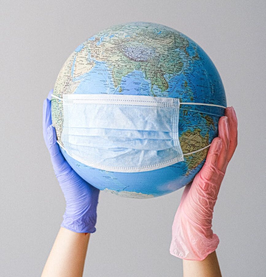 hands with latex gloves holding a globe with a face mask (Photo by Anna Shvets)