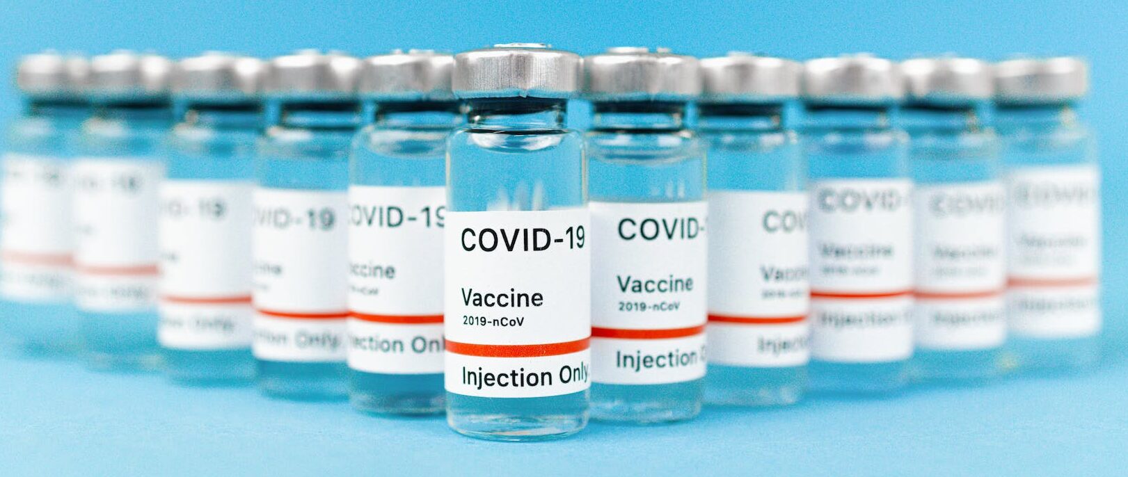 COVID-19 vaccine bottles on blue background (Photo by Maksim Goncharenok)