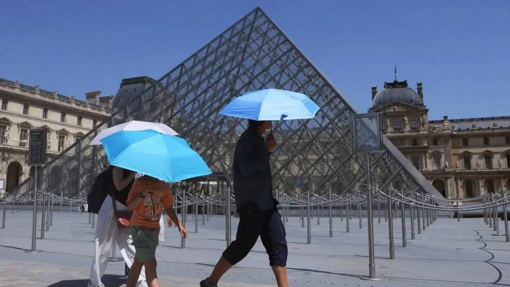 Tourists with umbrellas outside the Pyramid of the Louvre museum as it closes early due to the heatwave (Reuters)